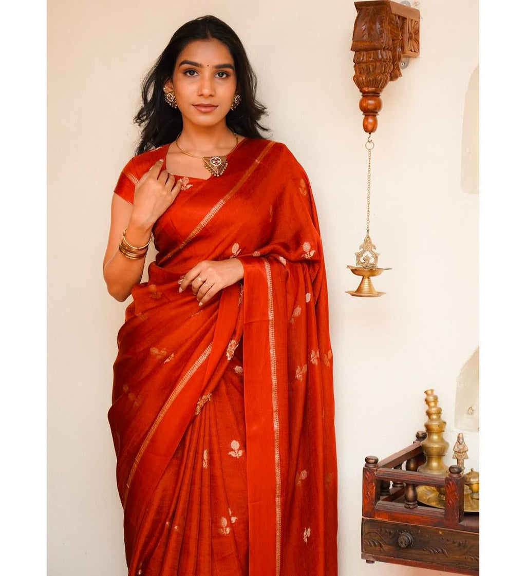 Woman wearing a red saree with gold patterns against a neutral background